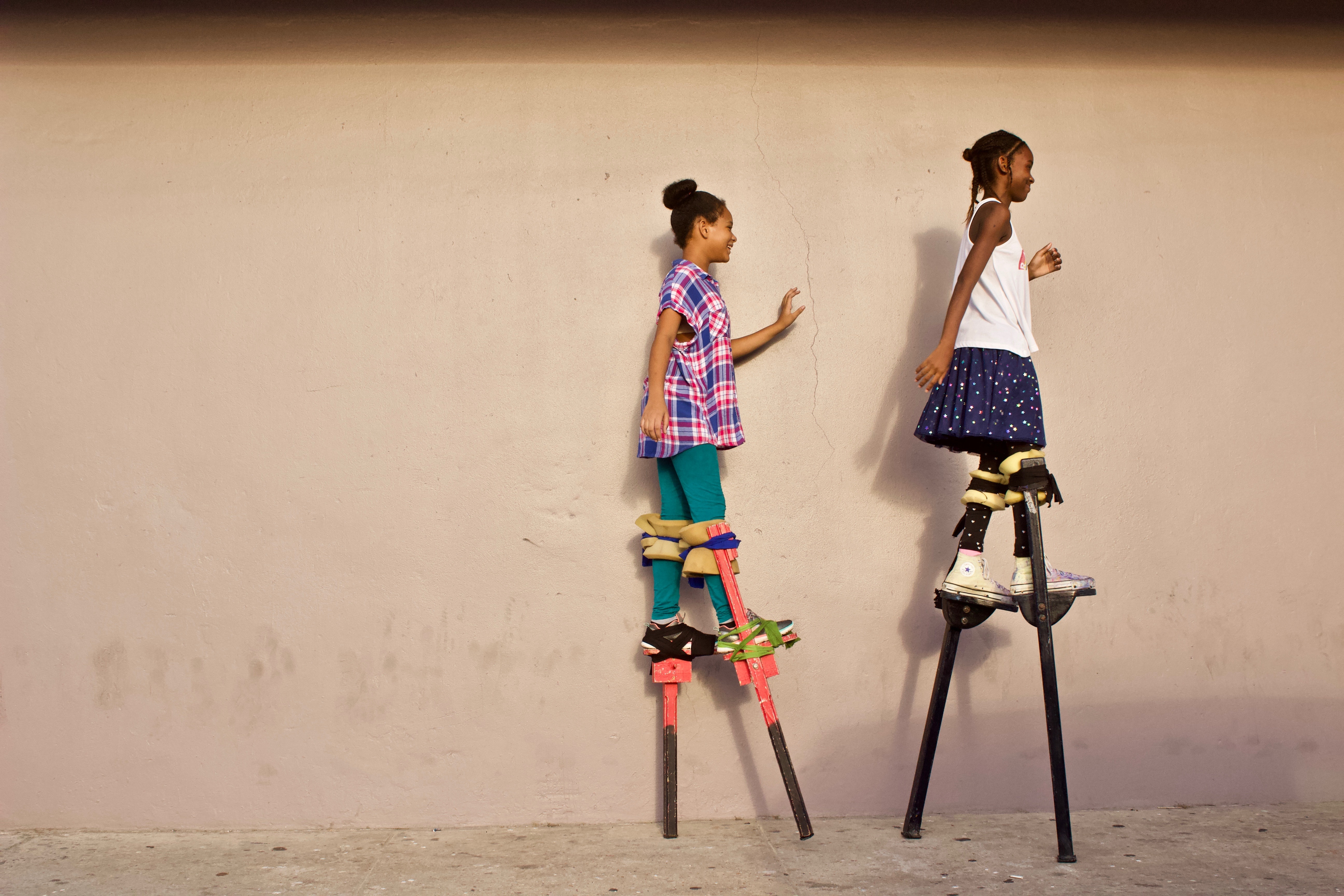 Photo of two girls walking on stilts next to a wall by Wayne Lee-Sing from Unsplash